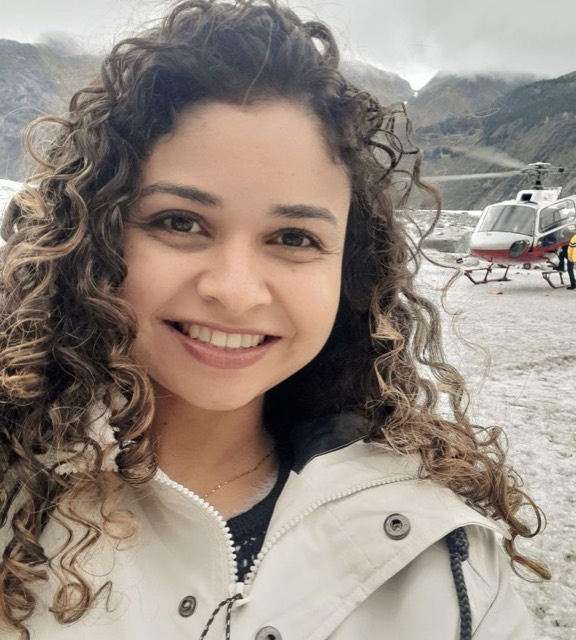 Teacher Hellen Azevedo sorrindo, com uma geleira e um helicóptero ao fundo